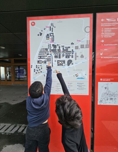 Deux enfants qui regardent un plan de situation et pointent du doigt le lieu où ils veulent aller.