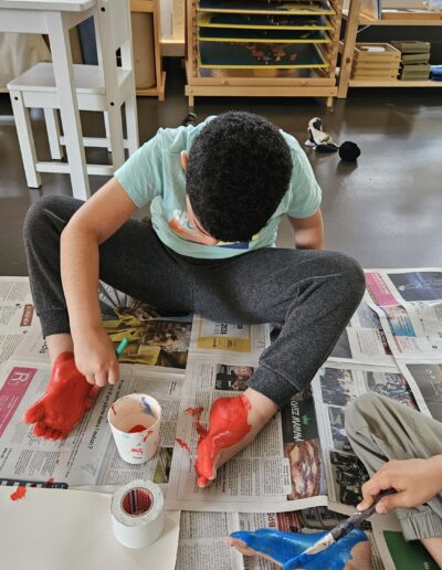 Un enfant assis par terre sur un papier journal qui met de la peinture rouge sous son pied.
