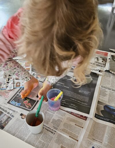 Un enfant assis par terre sur un papier journal qui met de la peinture sous son pied.