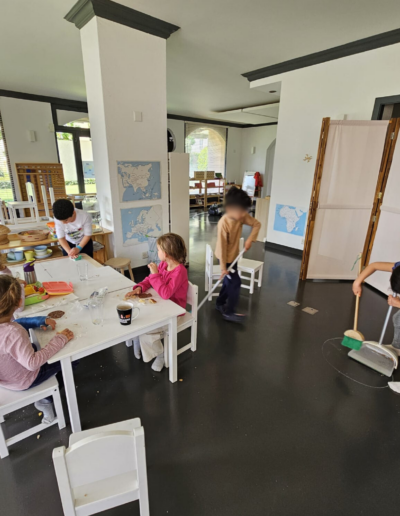 Deux enfants qui nettoient le sol de la salle de classe et 4 enfants autour d'une table qui terminent leur goûter.