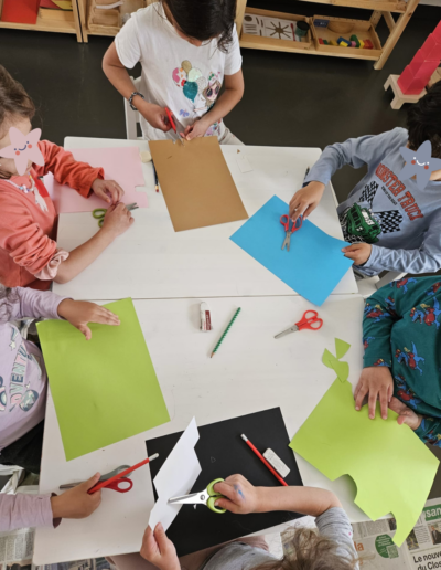 Six enfants assis autour d'une table qui font du découpage de feuilles colorées.