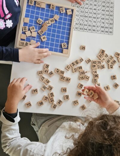 Deux petites filles assises à une table qui jouent avec un plateau de jeu couverte de pièces en bois avec des chiffres.